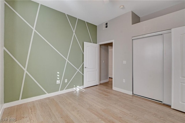 unfurnished bedroom featuring baseboards, a closet, visible vents, and wood finished floors