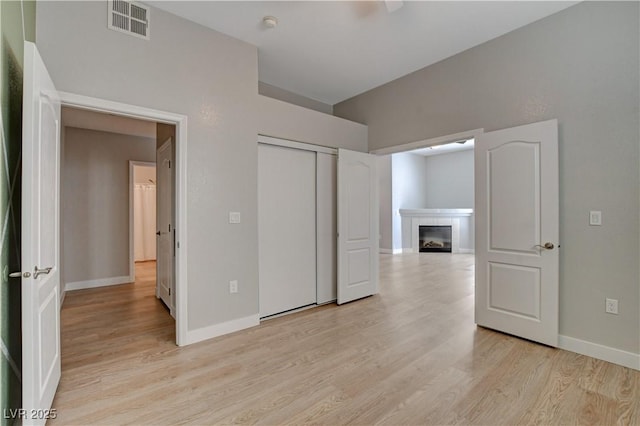 unfurnished bedroom with light wood-style flooring, a tiled fireplace, visible vents, and baseboards