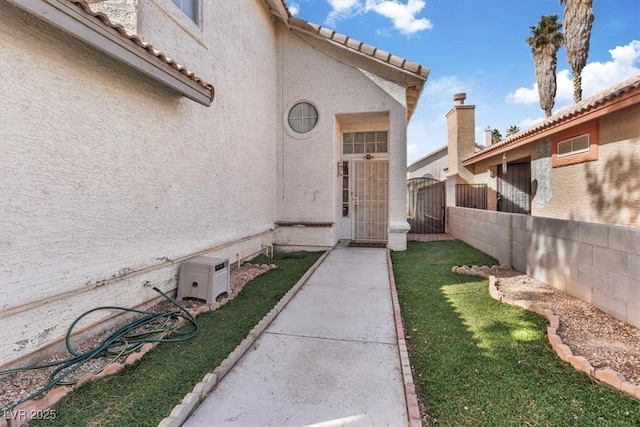 doorway to property with a tile roof, stucco siding, a lawn, a gate, and fence