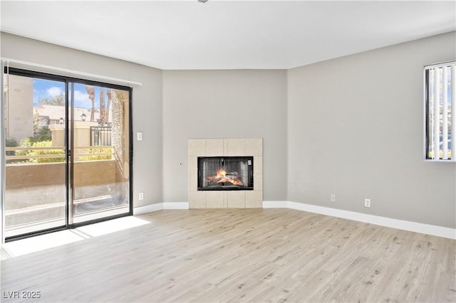 unfurnished living room featuring baseboards, a tiled fireplace, and light wood-style floors