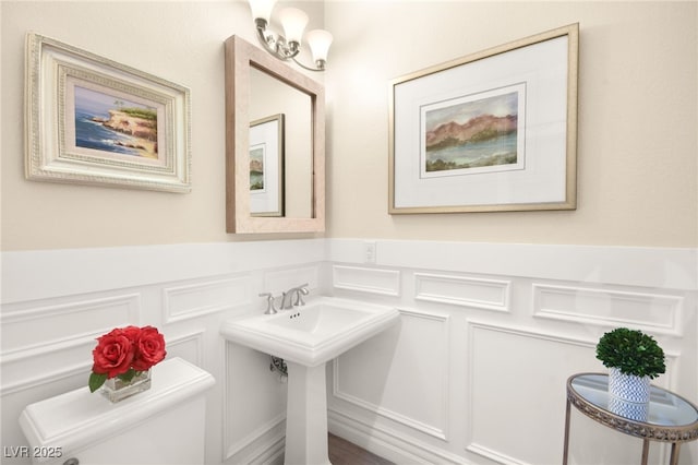 bathroom featuring a decorative wall, toilet, and wainscoting