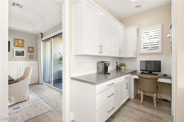 kitchen with visible vents, white cabinets, light wood-style flooring, and a wainscoted wall