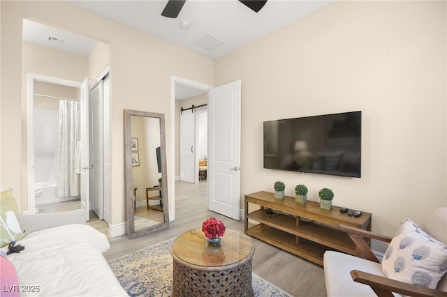 living area with light wood finished floors, visible vents, ceiling fan, baseboards, and a barn door