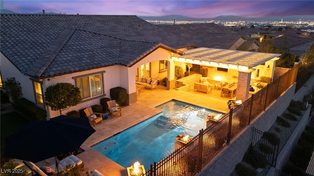 back of house at dusk with a fenced in pool, fence, a tiled roof, an outdoor hangout area, and a patio area