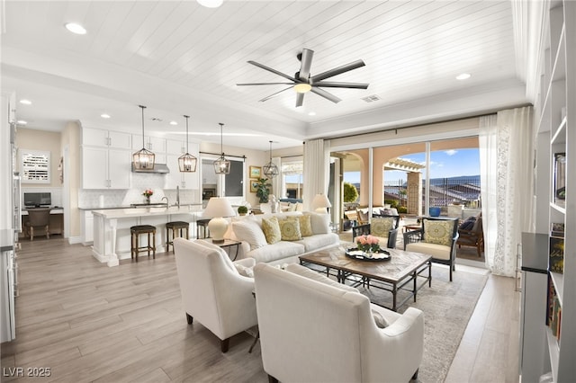 living room with visible vents, light wood-style floors, a ceiling fan, and crown molding