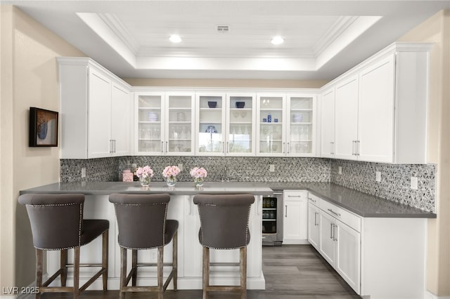 kitchen with white cabinets, a kitchen breakfast bar, a raised ceiling, and ornamental molding