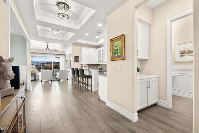 hallway with wood finished floors, a tray ceiling, recessed lighting, crown molding, and a decorative wall