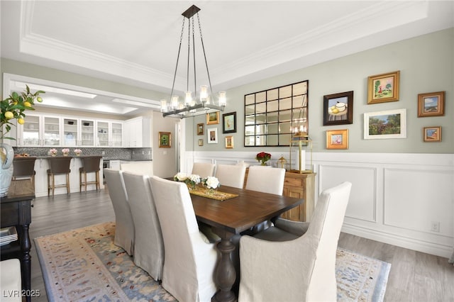 dining area featuring a tray ceiling, a wainscoted wall, and wood finished floors