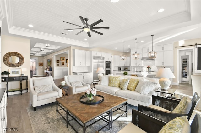 living area featuring crown molding, light wood-type flooring, a raised ceiling, and a barn door