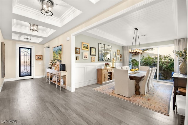 dining area with ornamental molding, wood finished floors, an inviting chandelier, a decorative wall, and a raised ceiling