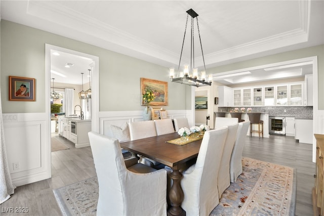 dining area with wine cooler, a chandelier, a tray ceiling, and a wainscoted wall