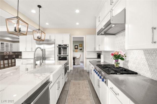 kitchen with under cabinet range hood, light stone counters, backsplash, wood finished floors, and stainless steel appliances