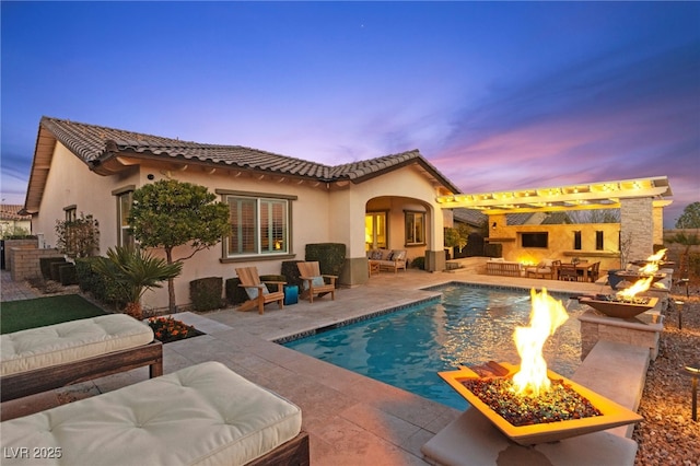 back of property at dusk featuring a tiled roof, stucco siding, an outdoor living space with a fire pit, and a patio area