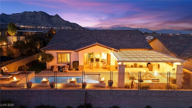 back of property at dusk with a patio, a fenced backyard, stucco siding, a tiled roof, and a mountain view