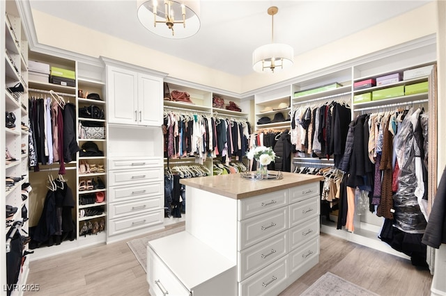 walk in closet with light wood finished floors and an inviting chandelier