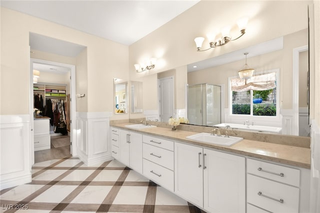 full bath with a sink, a wainscoted wall, a walk in closet, and a shower stall