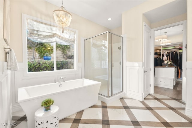 bathroom with a spacious closet, wainscoting, a stall shower, recessed lighting, and a soaking tub