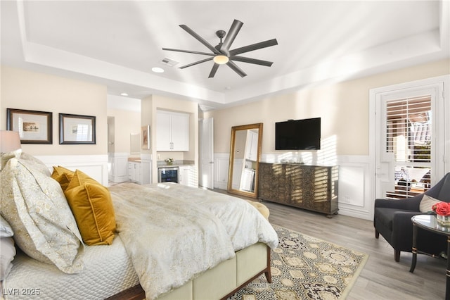 bedroom with a tray ceiling, beverage cooler, visible vents, and light wood finished floors