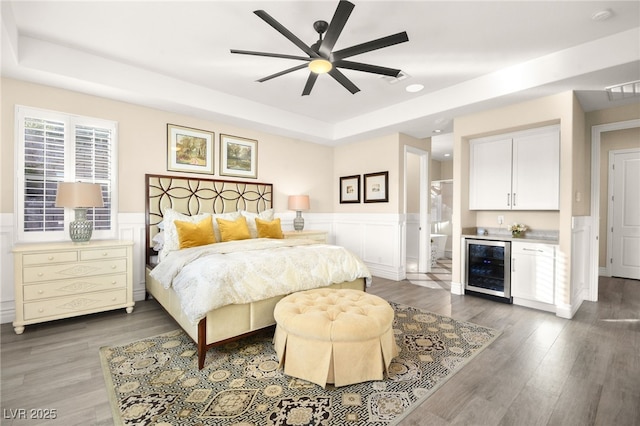 bedroom featuring a bar, a raised ceiling, wine cooler, and wood finished floors