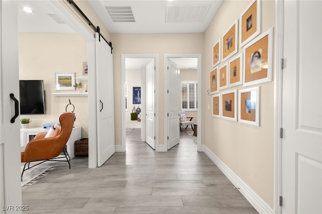 hall featuring a barn door, light wood-style floors, visible vents, and baseboards