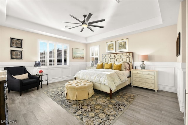 bedroom with a tray ceiling, a wainscoted wall, and wood finished floors