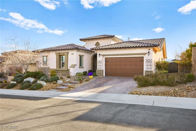 mediterranean / spanish house with a gate, stucco siding, a garage, a tiled roof, and decorative driveway