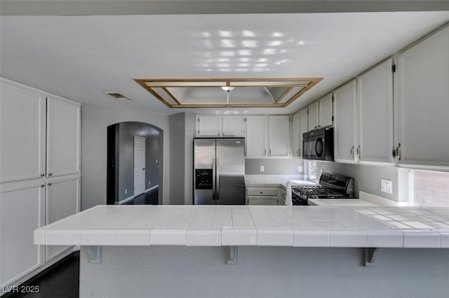 kitchen featuring a peninsula, black microwave, stainless steel fridge, and tile counters