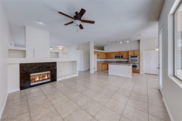 unfurnished living room featuring light tile patterned floors, ceiling fan, baseboards, and a tile fireplace