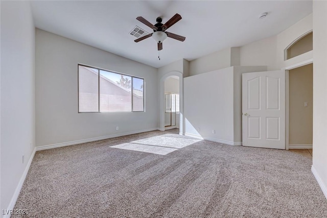 spare room with arched walkways, light carpet, visible vents, a ceiling fan, and baseboards