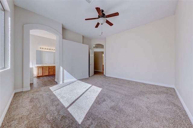 interior space with arched walkways, ensuite bathroom, carpet flooring, ceiling fan, and baseboards