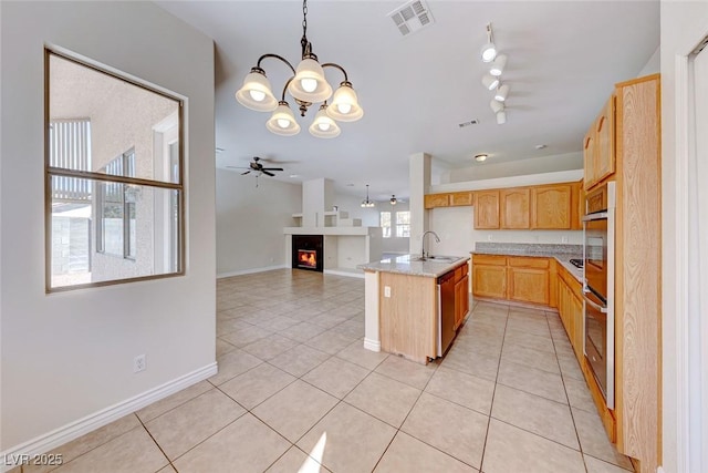 kitchen featuring light stone counters, pendant lighting, light tile patterned floors, open floor plan, and a sink