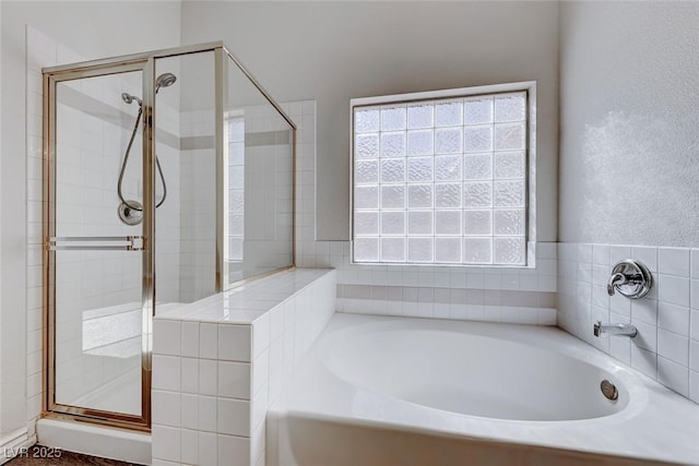 bathroom with a textured wall, a shower stall, and a bath