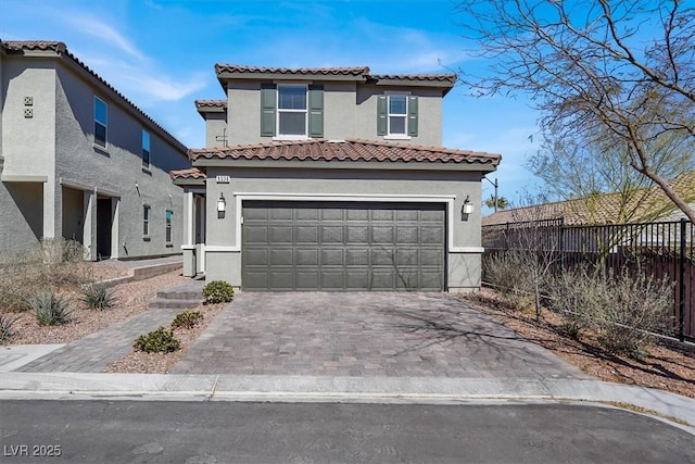 mediterranean / spanish-style home with an attached garage, fence, a tile roof, decorative driveway, and stucco siding