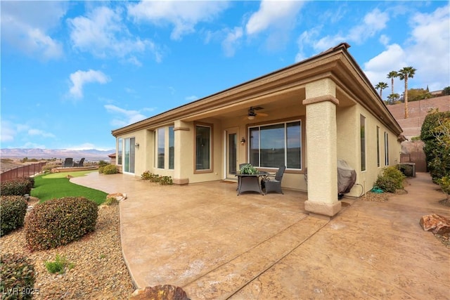 back of property with stucco siding, fence, a mountain view, ceiling fan, and a patio area