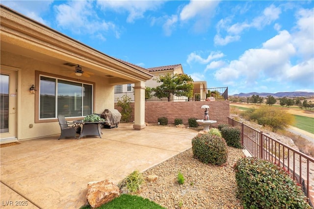 view of patio with a mountain view, a ceiling fan, and fence