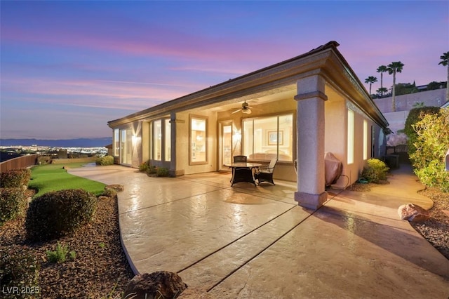 back of house at dusk featuring stucco siding, a patio, and a ceiling fan