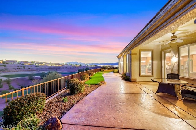 patio terrace at dusk featuring a ceiling fan and fence