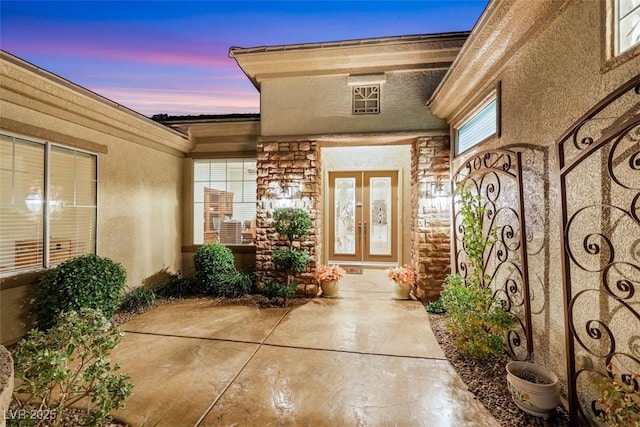 entrance to property with french doors, stone siding, and stucco siding