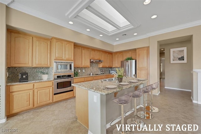 kitchen with under cabinet range hood, appliances with stainless steel finishes, a skylight, and light brown cabinetry