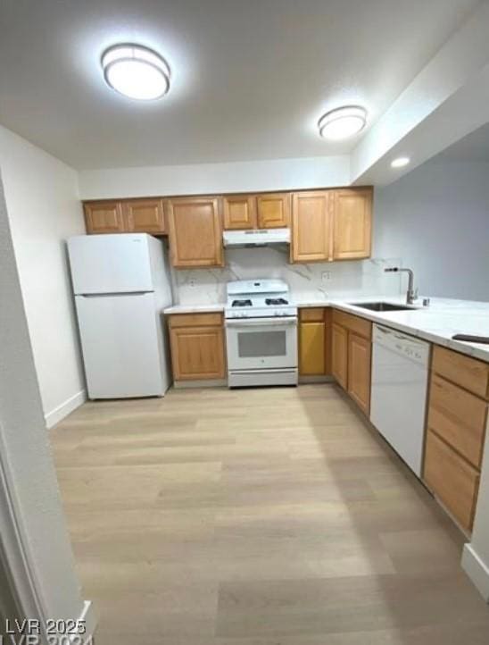 kitchen with under cabinet range hood, white appliances, a sink, light countertops, and brown cabinetry