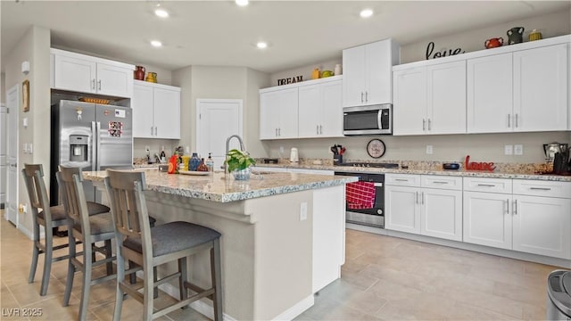 kitchen with appliances with stainless steel finishes, white cabinetry, and an island with sink