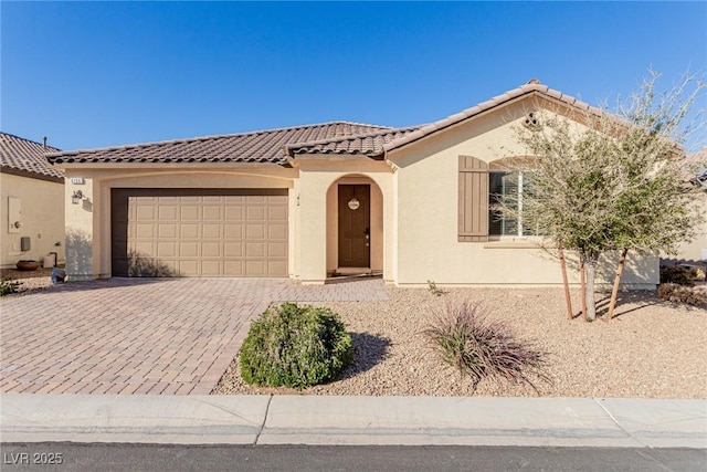 mediterranean / spanish home featuring decorative driveway, an attached garage, a tile roof, and stucco siding