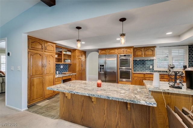 kitchen featuring stainless steel appliances, a raised ceiling, brown cabinets, and decorative backsplash