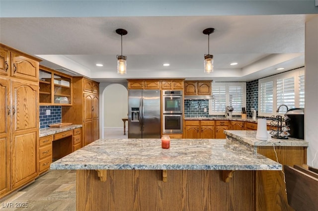 kitchen with stainless steel appliances, a tray ceiling, brown cabinetry, and built in study area