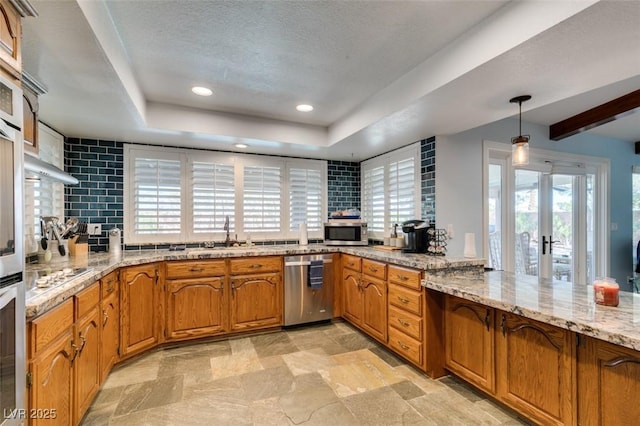 kitchen with appliances with stainless steel finishes, backsplash, light stone countertops, a tray ceiling, and brown cabinetry