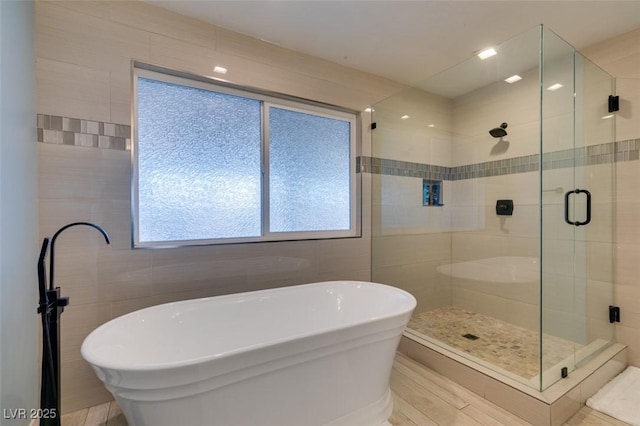 full bathroom with a freestanding tub, a shower stall, and tile walls