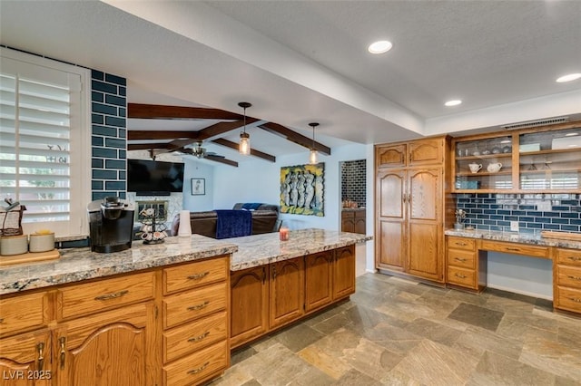 kitchen featuring light stone counters, tasteful backsplash, lofted ceiling with beams, a ceiling fan, and built in study area