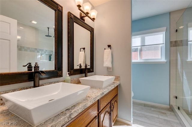 full bathroom featuring double vanity, a shower stall, baseboards, and a sink