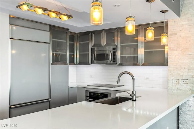 kitchen featuring stainless steel appliances, a sink, light countertops, glass insert cabinets, and pendant lighting