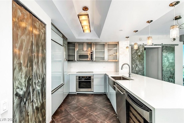 kitchen featuring a barn door, glass insert cabinets, hanging light fixtures, a peninsula, and stainless steel appliances